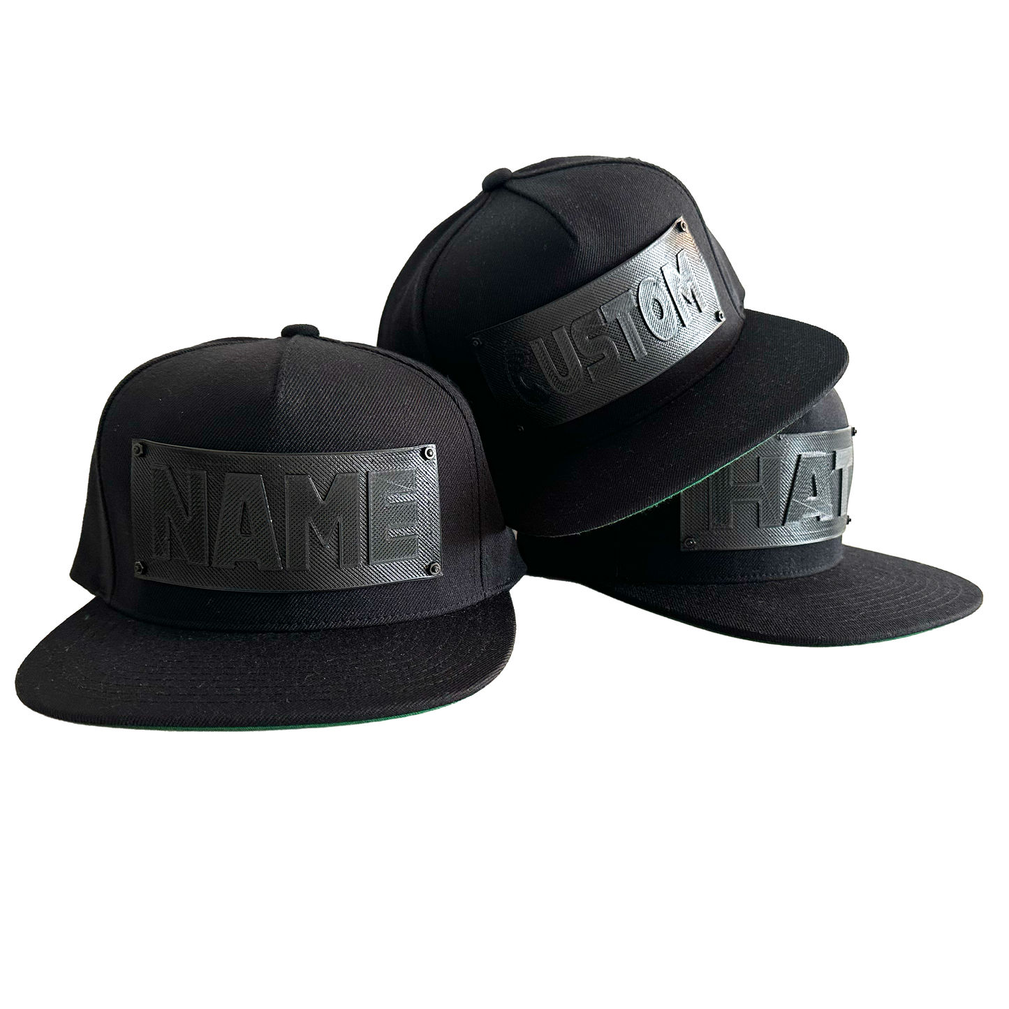 3 snapback baseball caps in black with black 3D printed logo panels. One says "CUSTOM",one says NAME", and the third says "HAT".