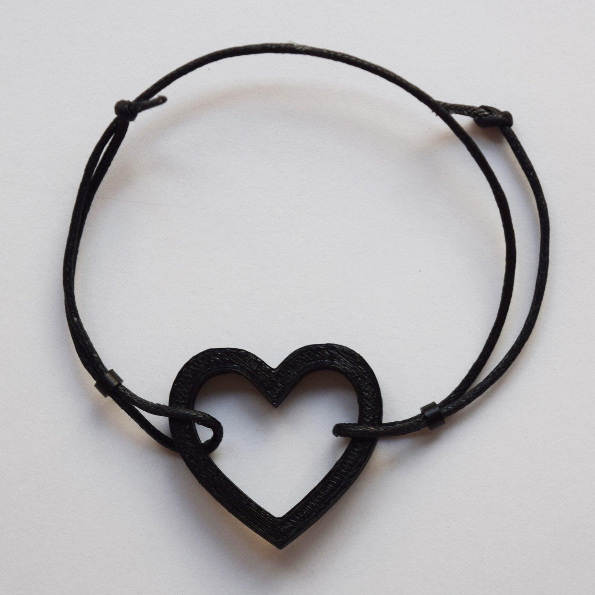 Bracelet made of a matte black colored 3D printed open heart shape and black waxed cotton thread