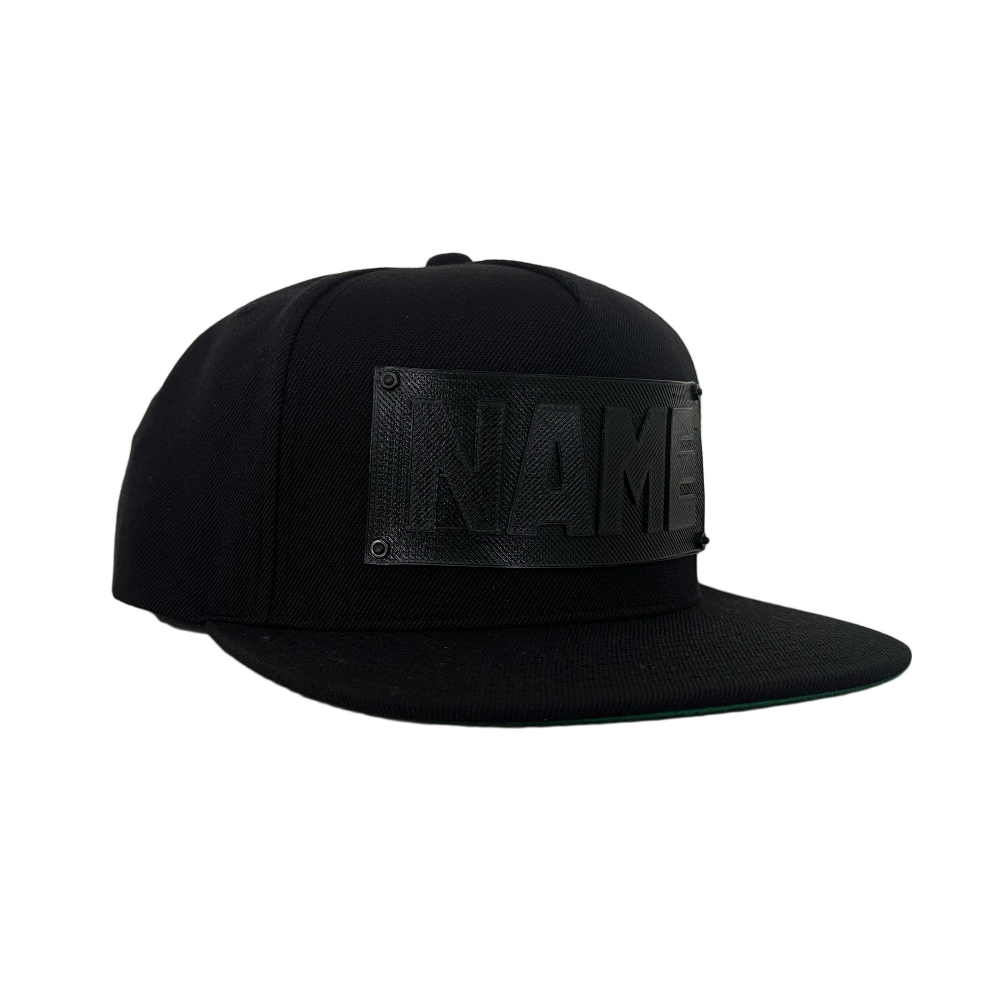 A black snapback baseball hat with a black logo panel that says"NAME".